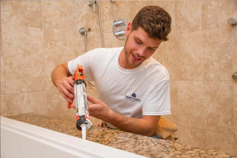 A skilled Prep'n Sell handyman applies caulk to seal a bathtub, ensuring a watertight bathroom fixture.