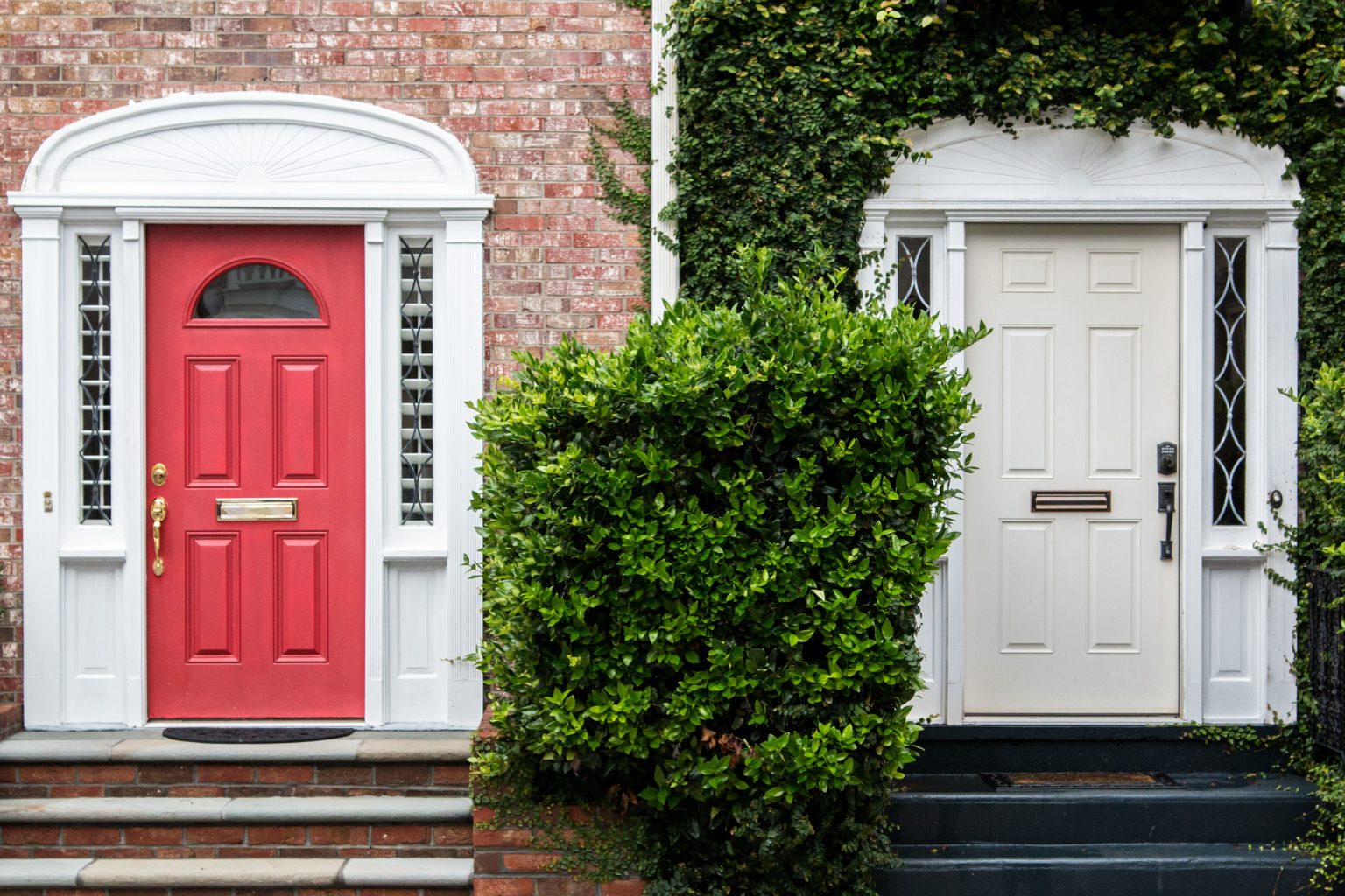 Two adjacent entrances, one with a red door and one with a cream door, both flanked by white framing and brickwork.