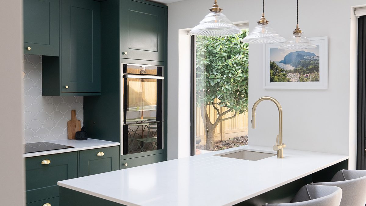 Elegant kitchen with dark green cabinets, brass fixtures, and a white countertop.