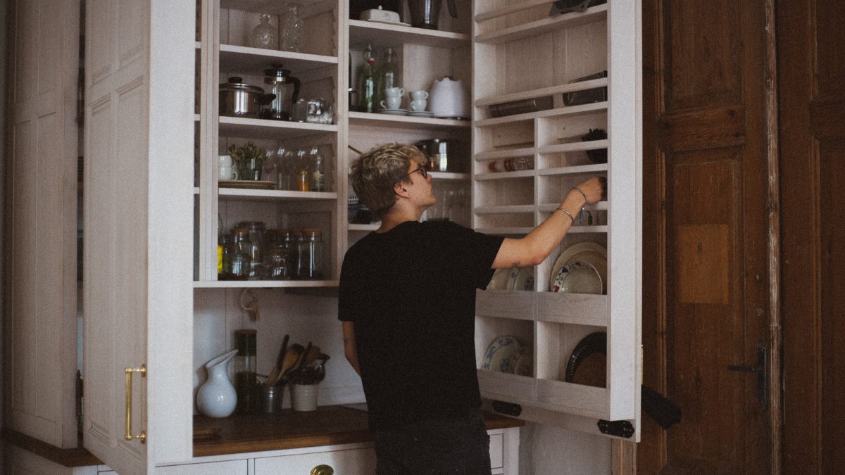 Person reaching for a dish in an open white shelved pantry.