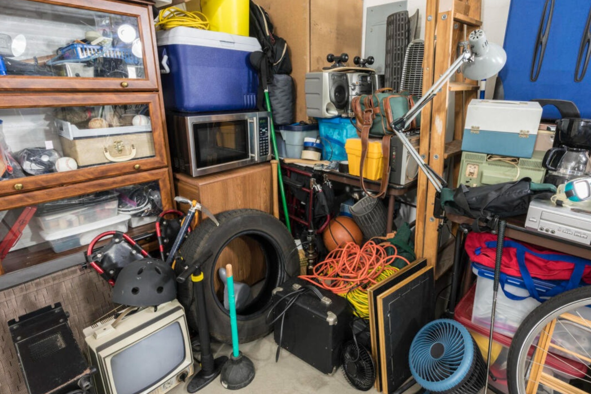 Garage overwhelmed with clutter, featuring boxes, old furniture, and various tools.