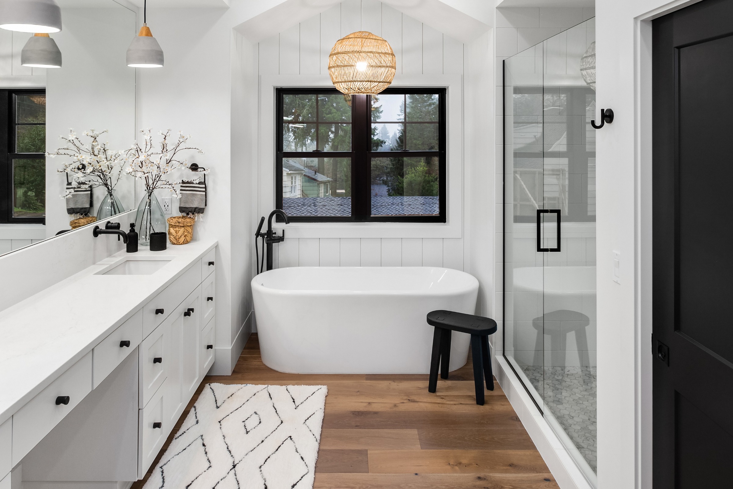 Modern bathroom with white freestanding tub, double vanity, and black accents.
